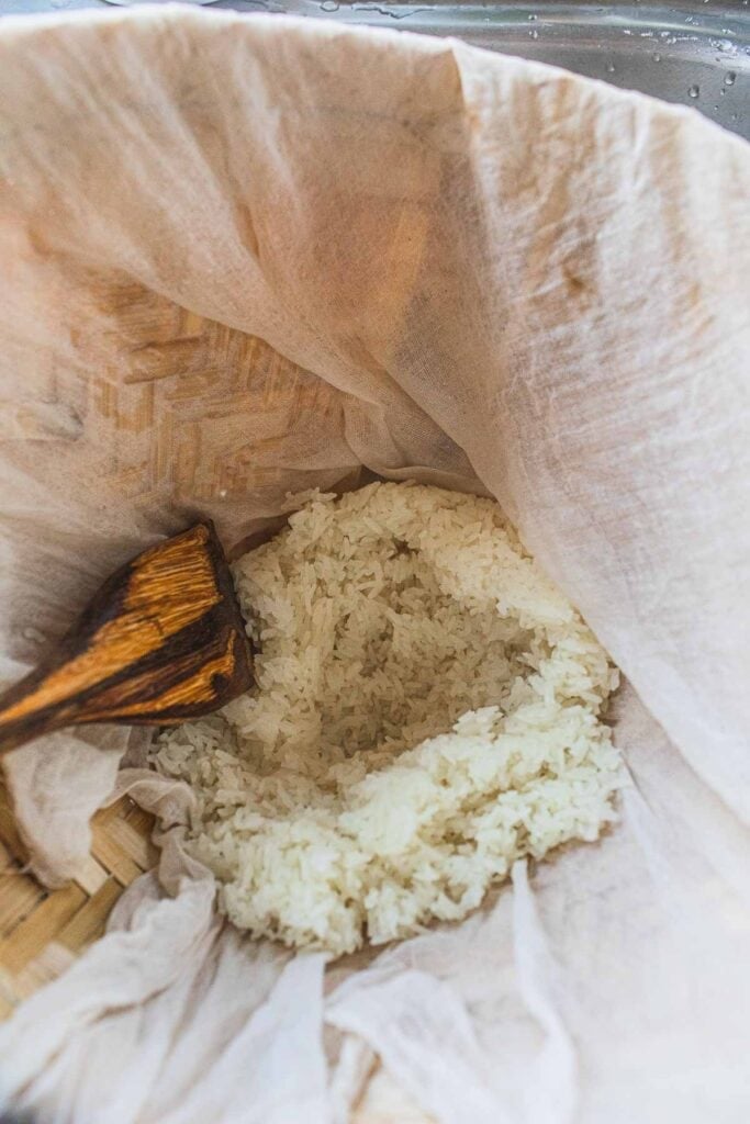 spoon fluffing Sticky rice in a bamboo basket.