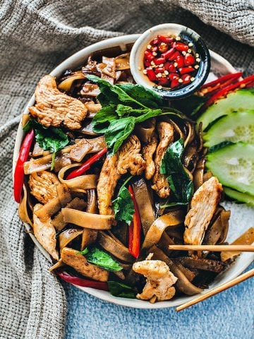 Drunken Noodles on a plate with chilis and cucumber garnish