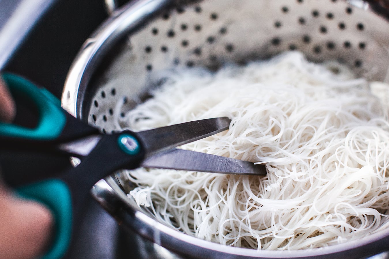 scissor cutting Rice noodles in a colander