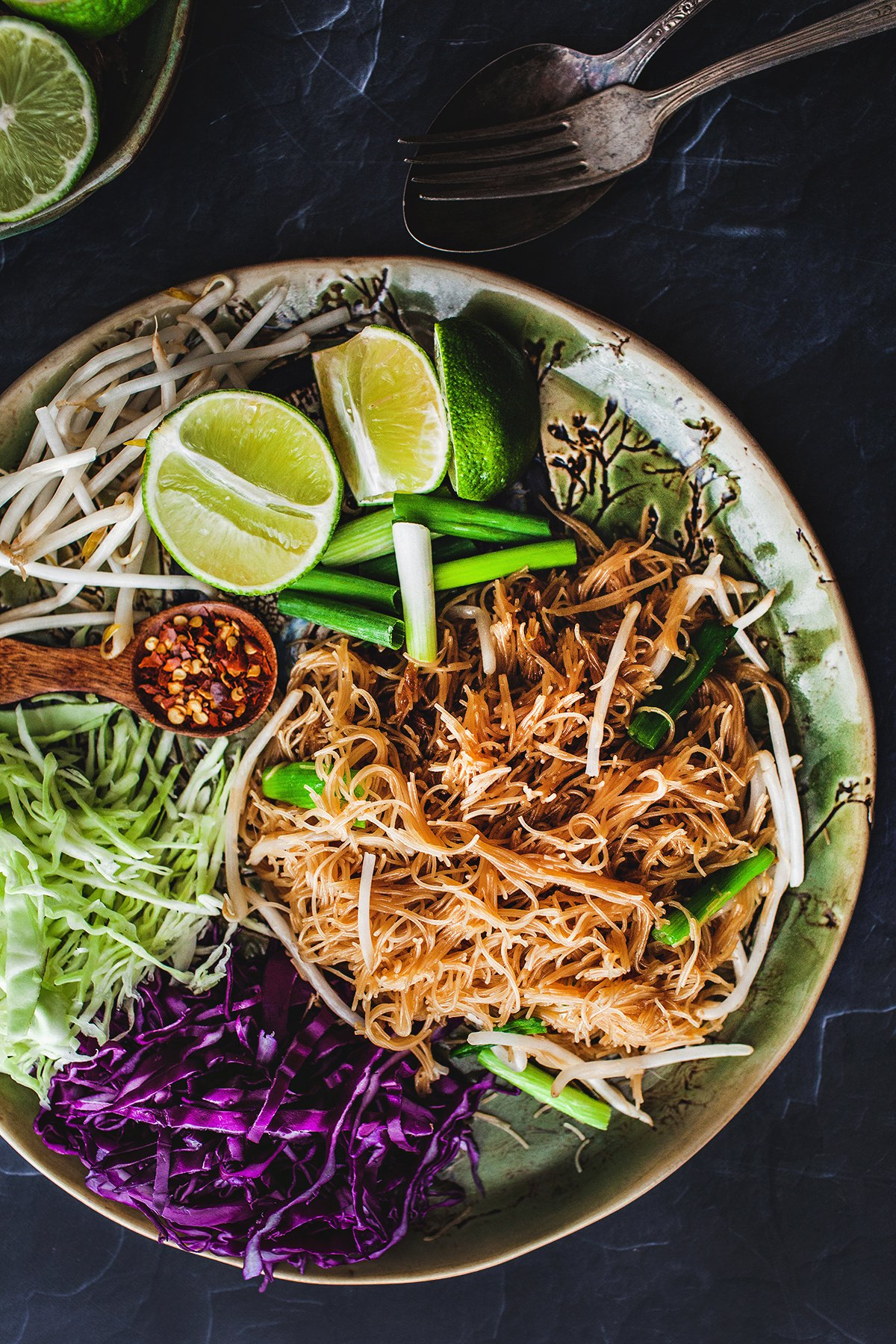 Pad Mee stir fry noodles on a plate with lime wedges and chili flakes garnish.