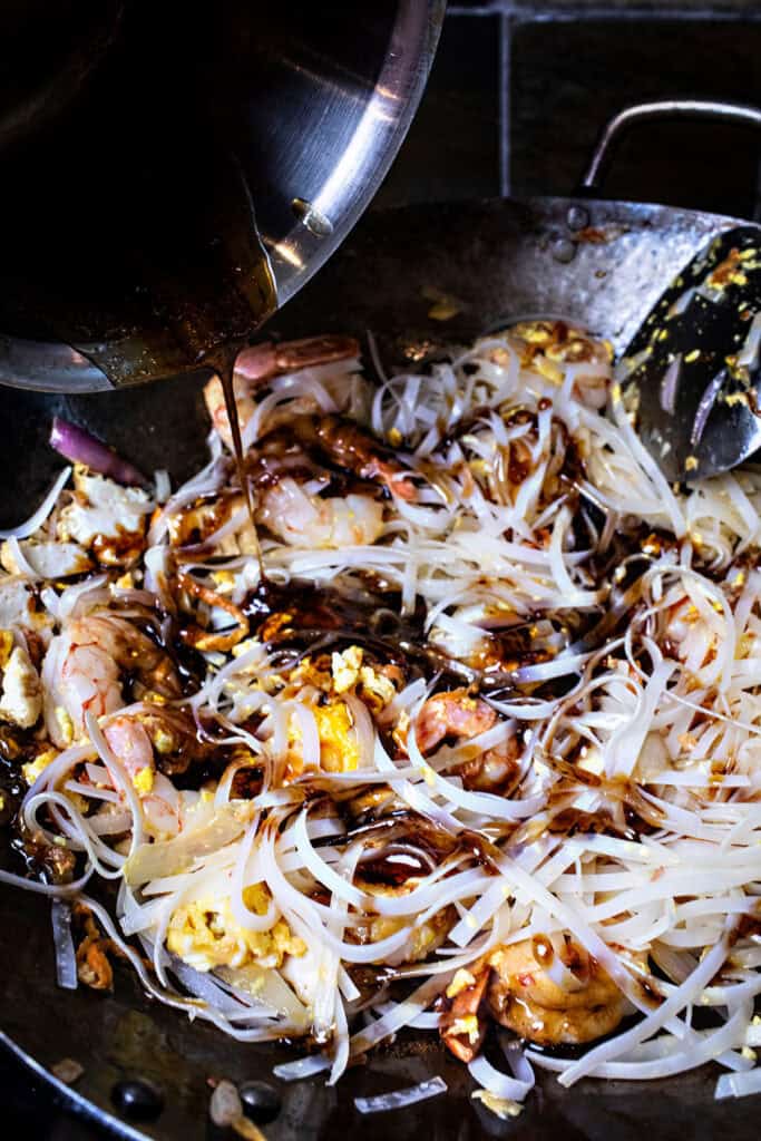 Sauce pouring over Rice noodles for pad thai in a wok. 