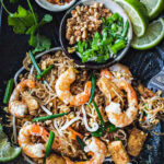 Shrimp pad Thai on a blue platter with garnishing on the side.