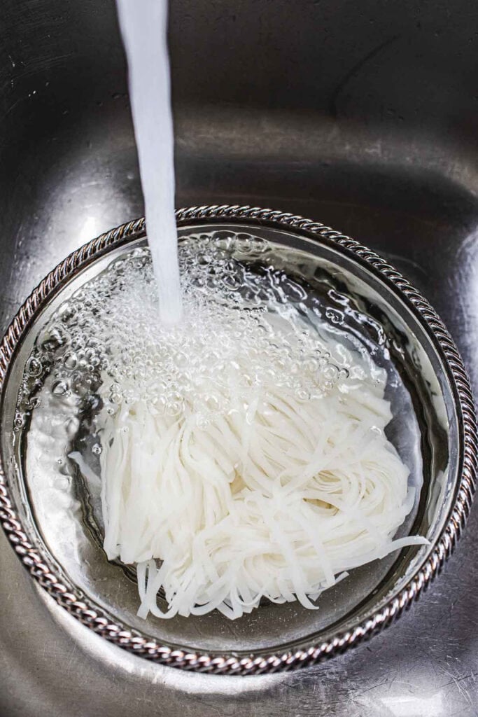Running water over Pad Thai noodles in a bowl.