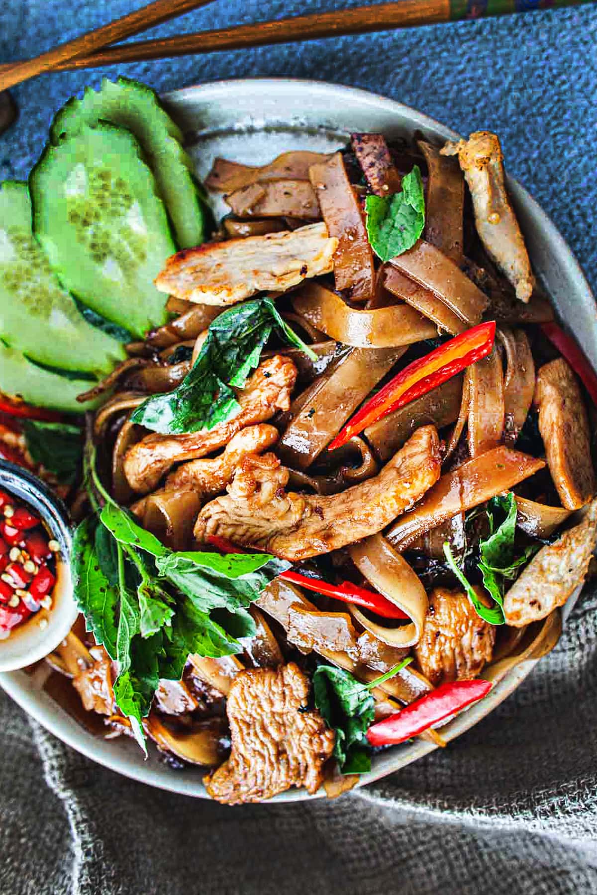 Thai chicken drunken noodles on a plate with cucumber slices