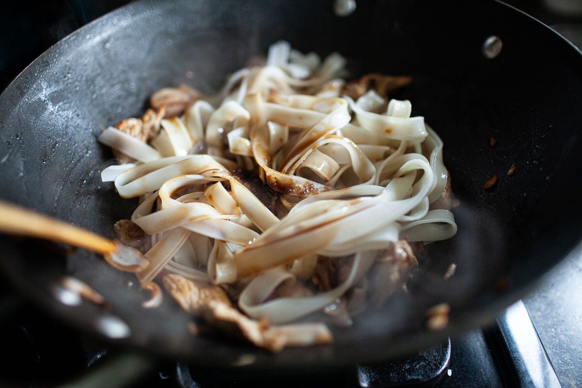 drunken noodles with sauce in a wok.