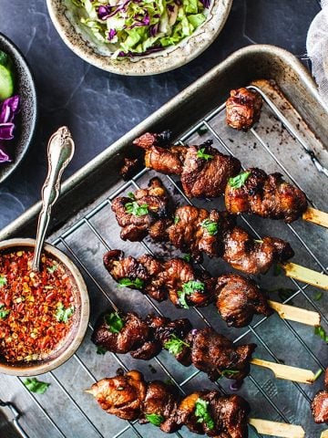 Thai grilled pork skewers on a tray with chili dipping sauce.