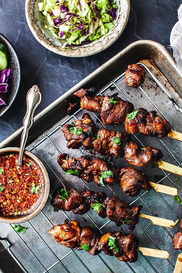 Thai grilled pork skewers on a tray with chili dipping sauce.