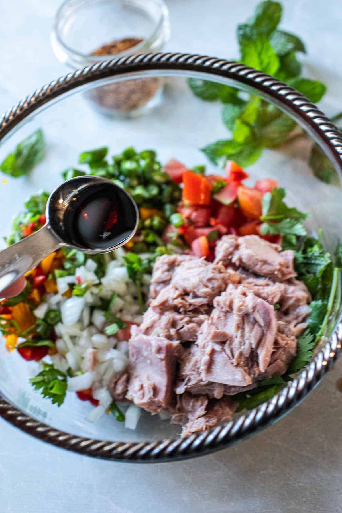 Thai Tuna salad in a bowl with sauce adding to it. 