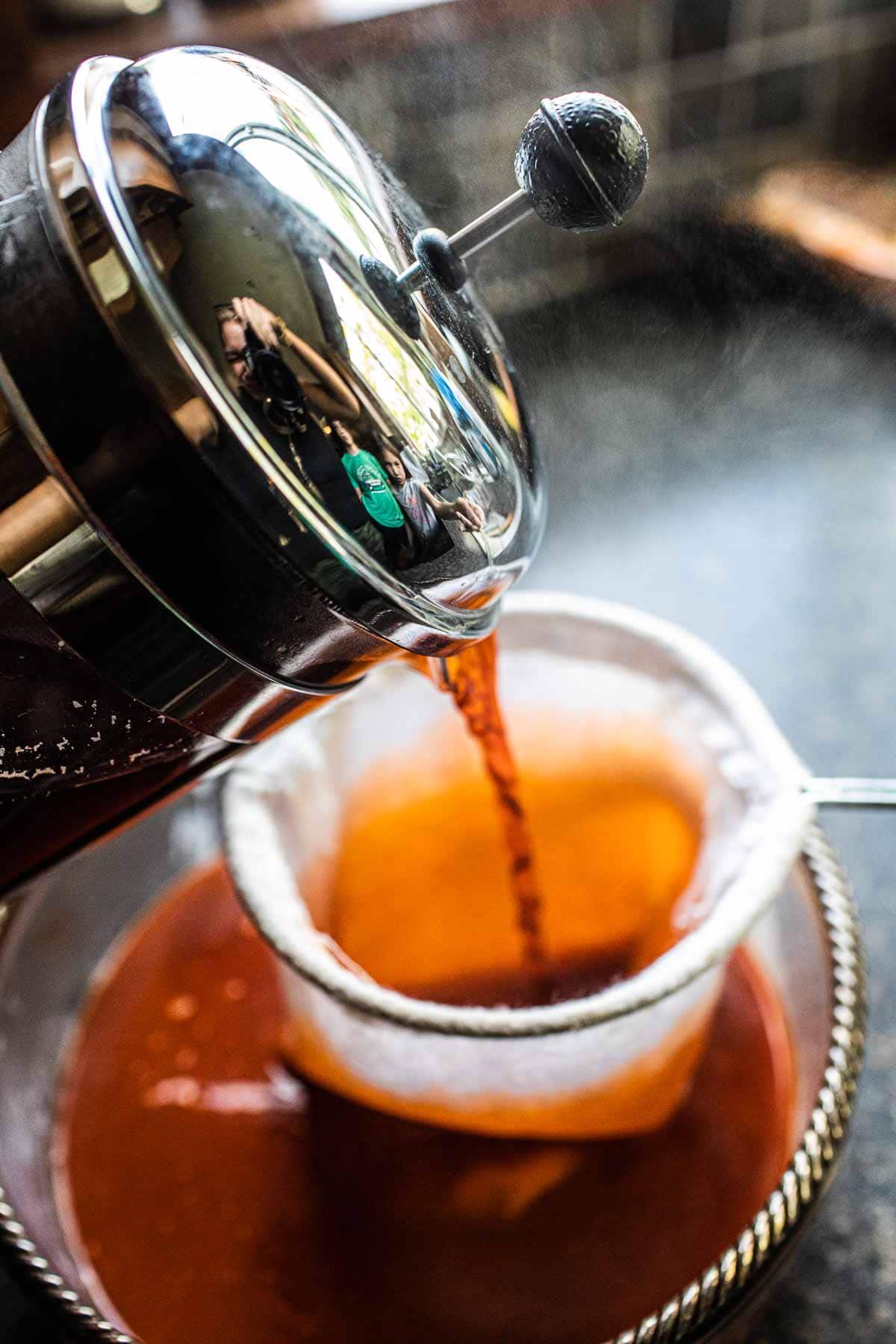 Thai iced tea straining in a tea sock in a bowl.