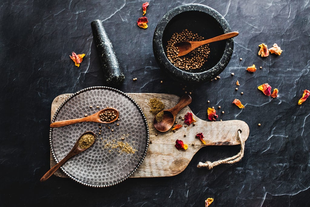 Spices in a small granite mortar and pestle on a table wit a cutting board.
