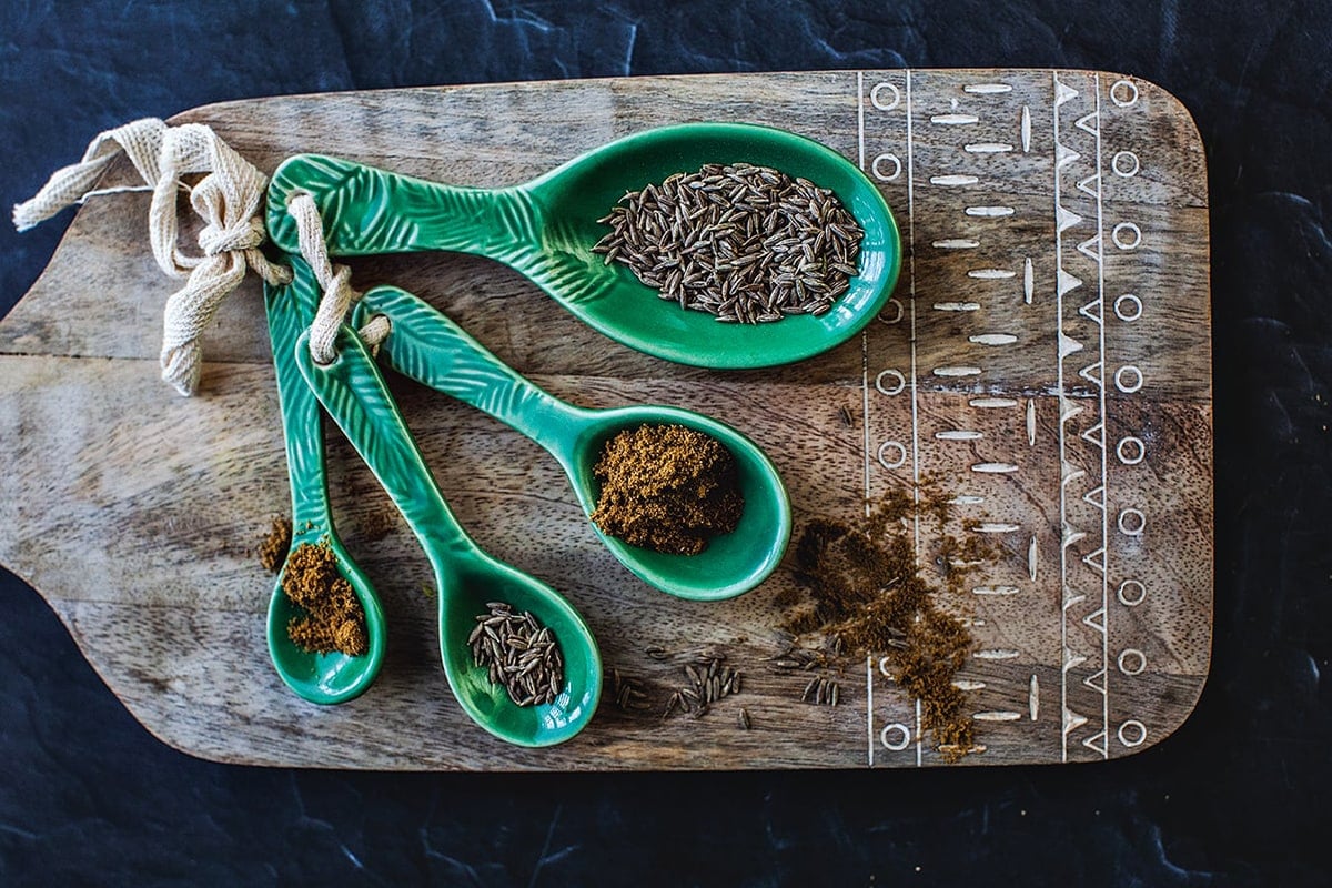 Ground and whole cumin in measuring spoons. 