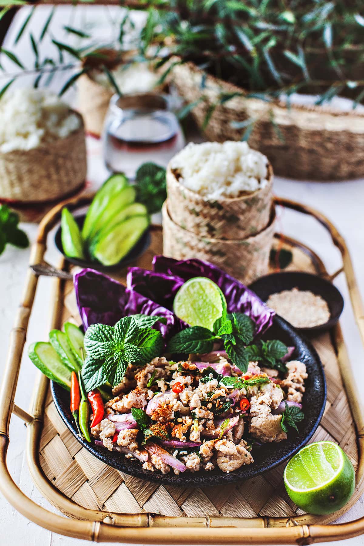 Larb Gai salad on a tray with sticky rice and sliced cucumbers. 