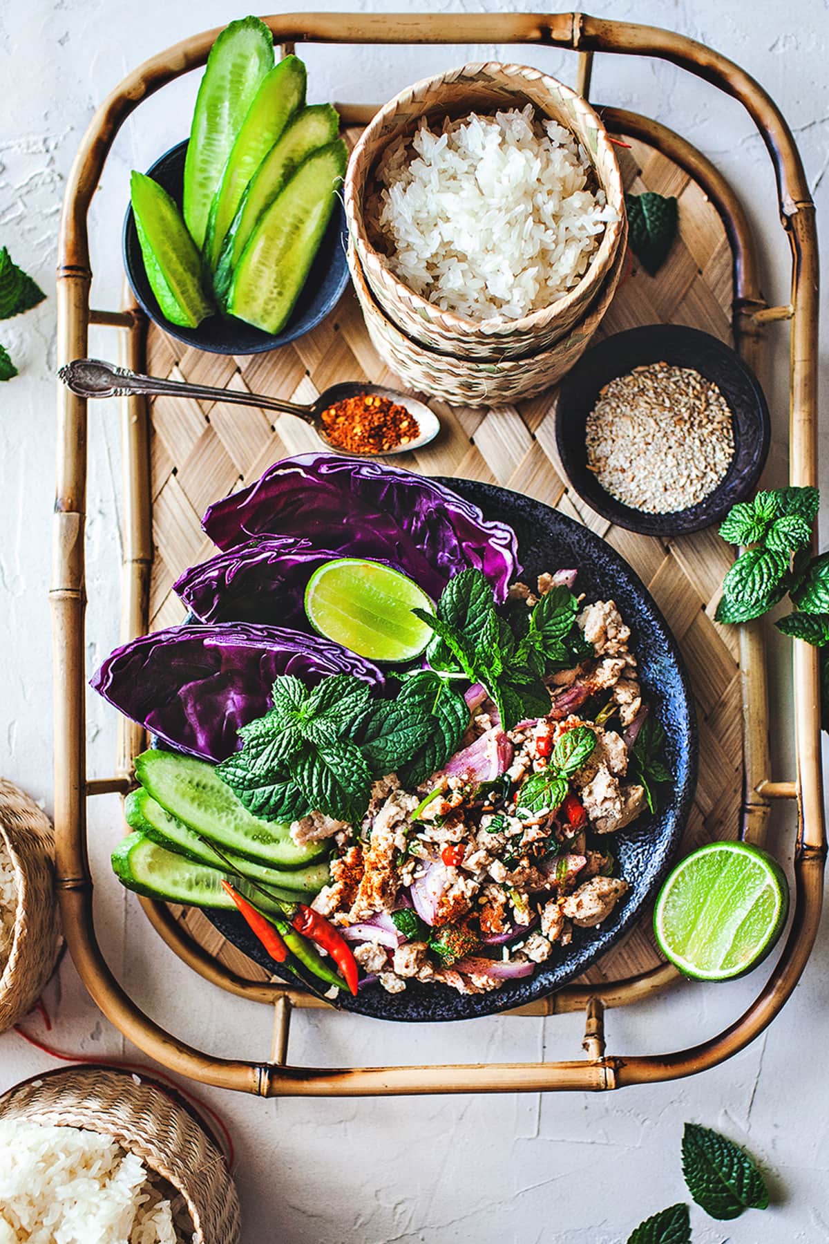 Larb gai on a plate with sticky rice and herbs on the side. 