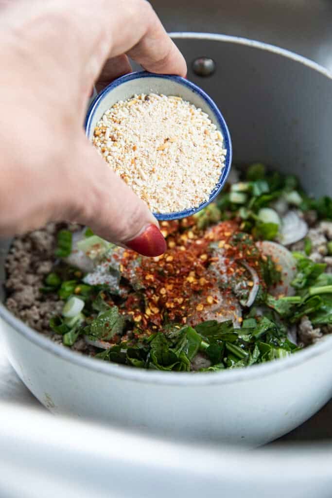 toasted rice powder added to Laab Gai \ in a pot with ground chicken, herbs and chilies.