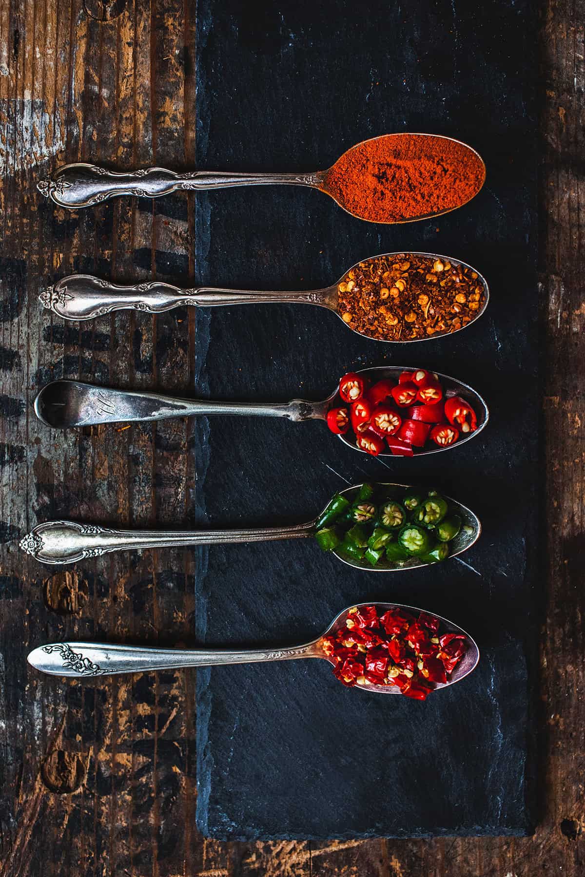 Thai chilis and chili flakes on spoons on the table.