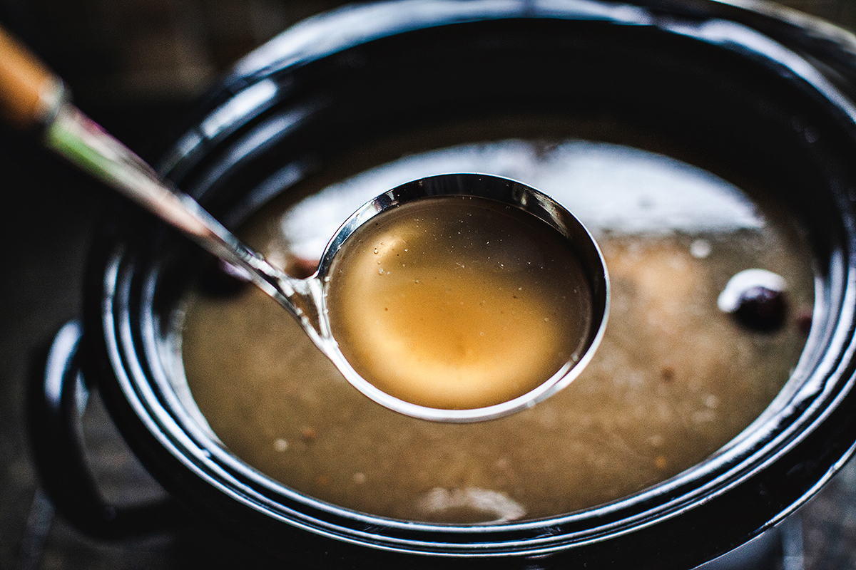 Spoon with bone broth over crock pot.