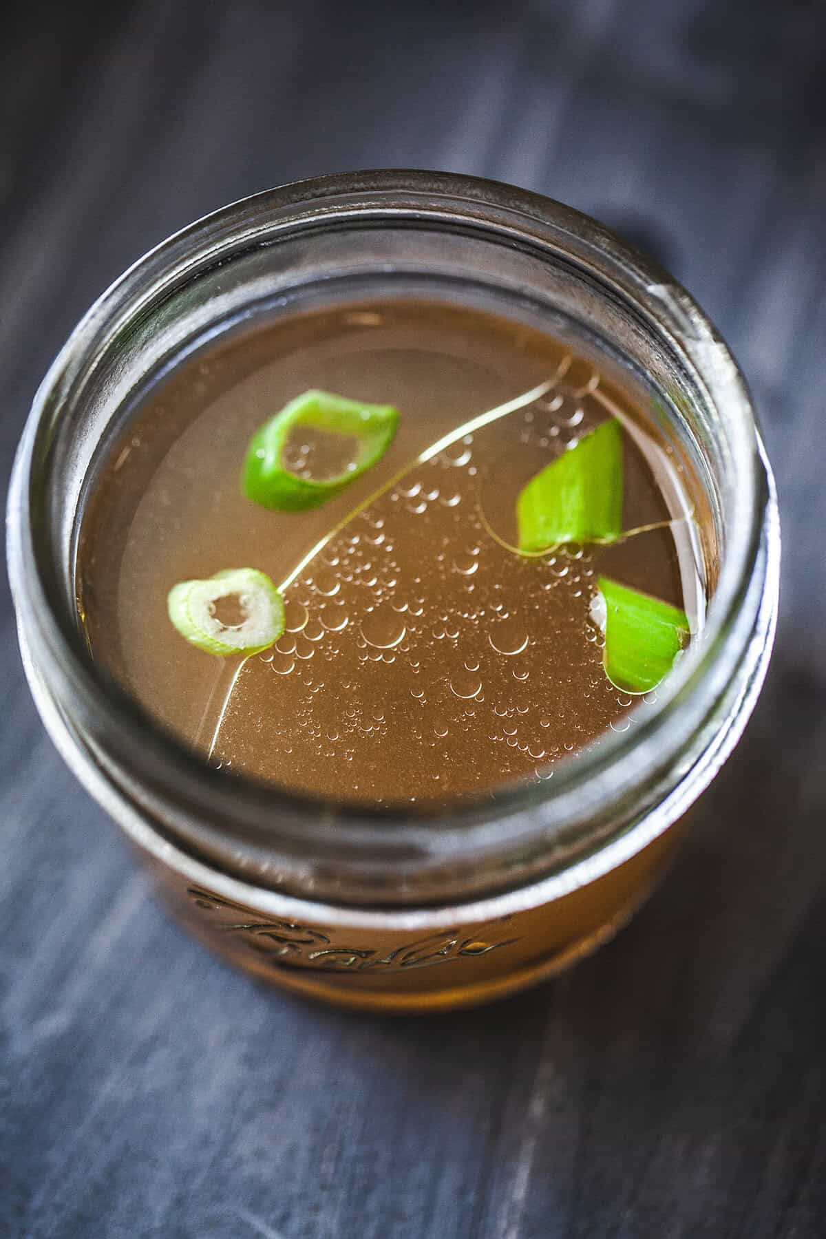 Bone broth in a mason jar with green onion garnish. 