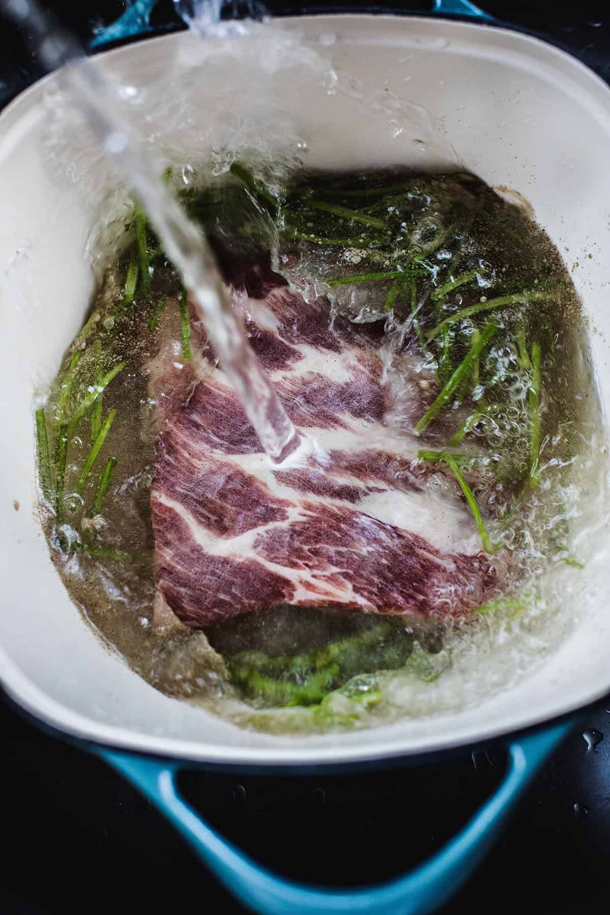 Water pouring into a pot with ribs and herbs.