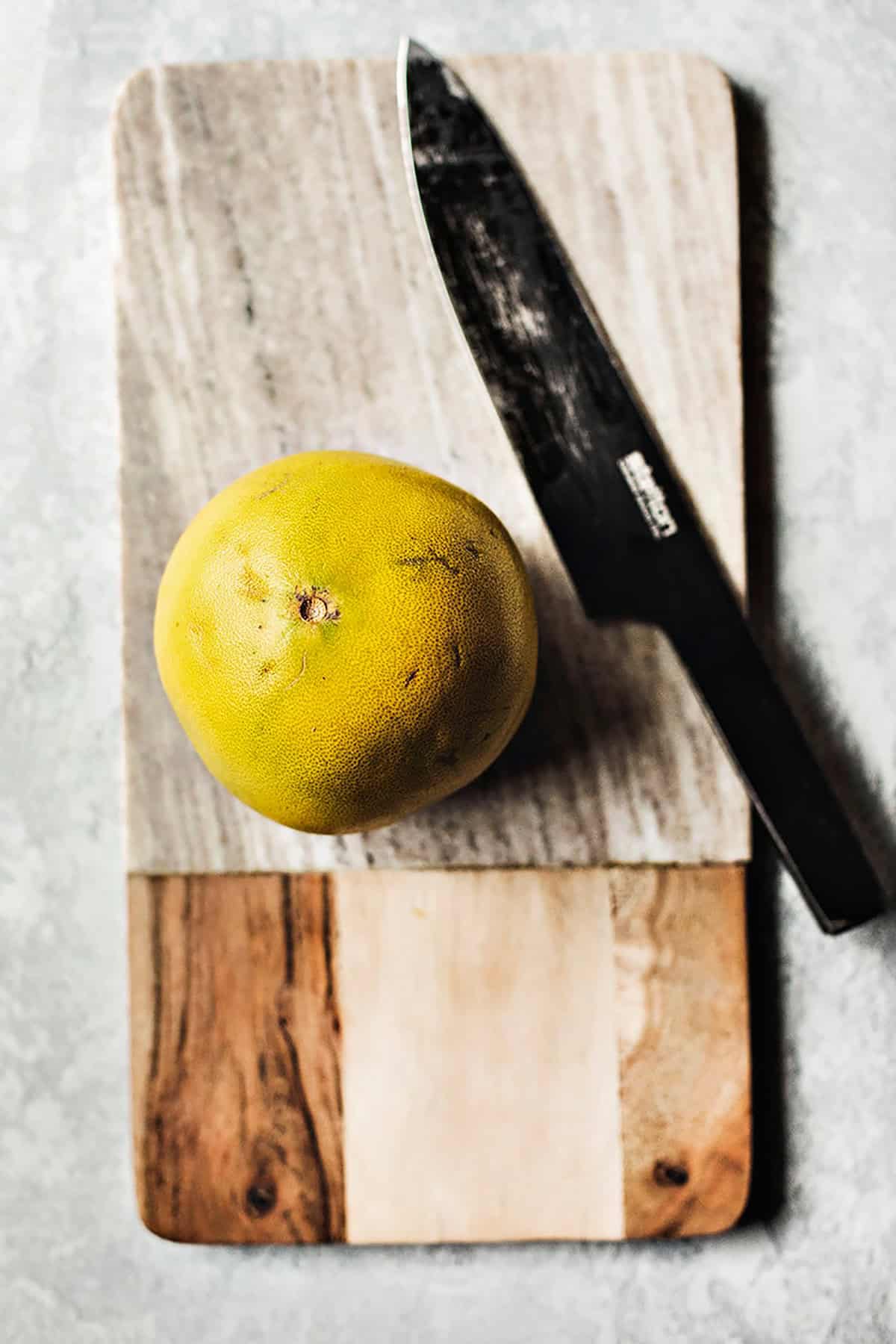 Sliced of a pomelo with a knife on a cutting board.