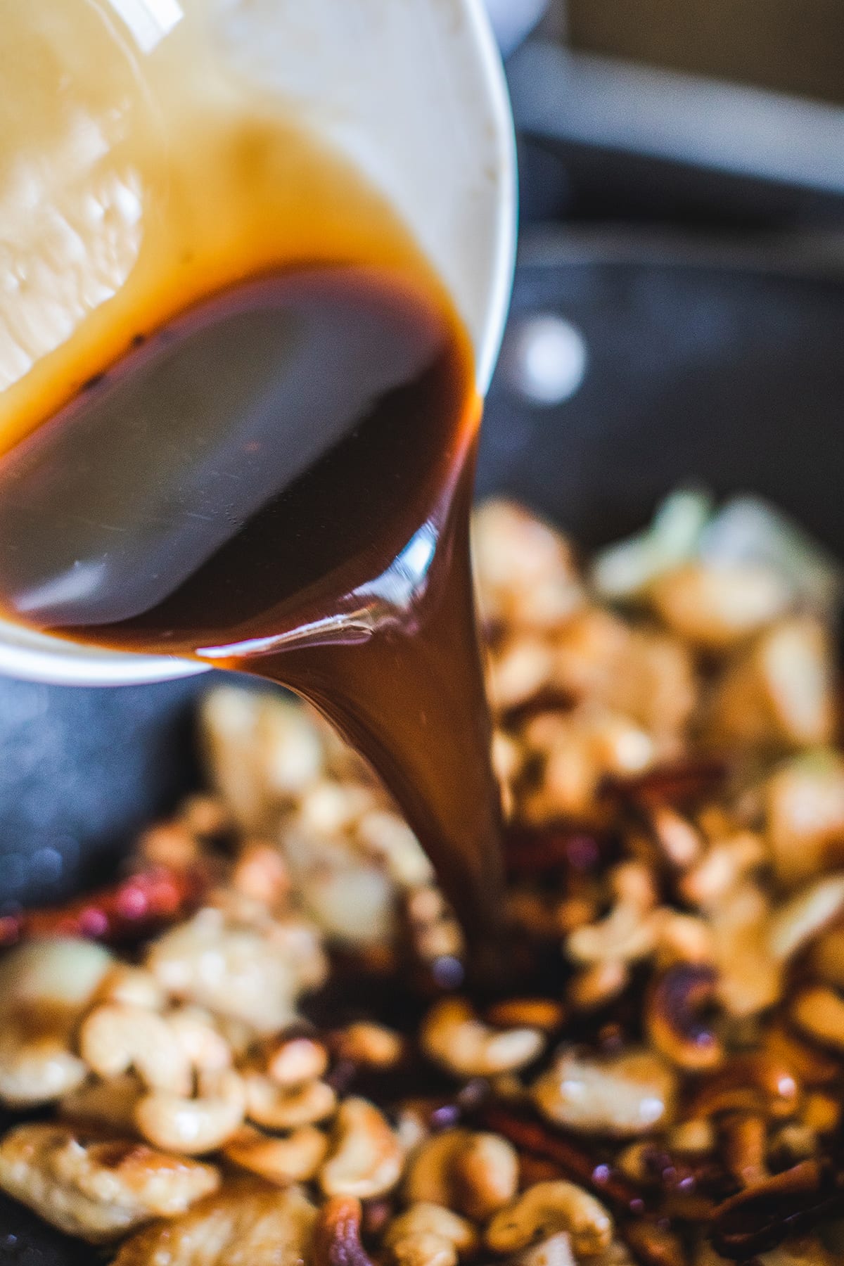 Cashew chicken sauce pouring into chicken in a wok.