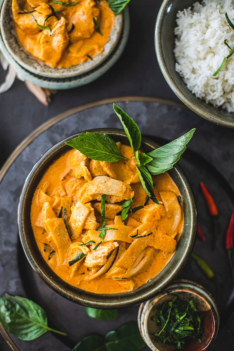 bowl of chicken thai red curry with basil garnish with rice and smaller bowl in background.