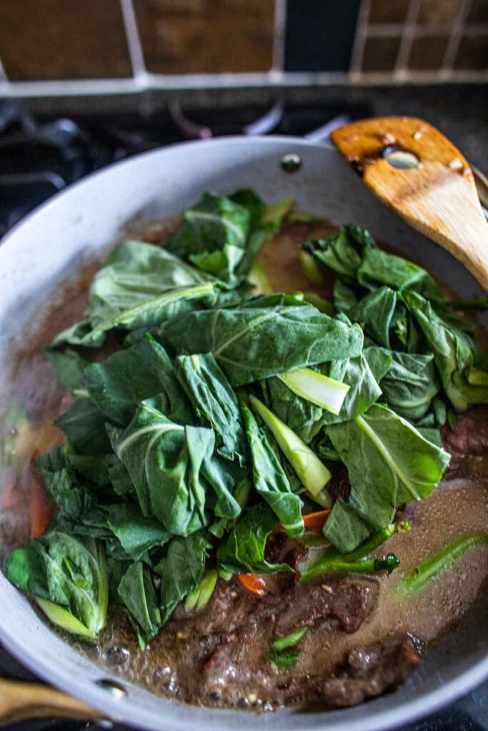 Thai Rad Na stir frying in a pan with beef, carrot and leafy Chinese broccoli.