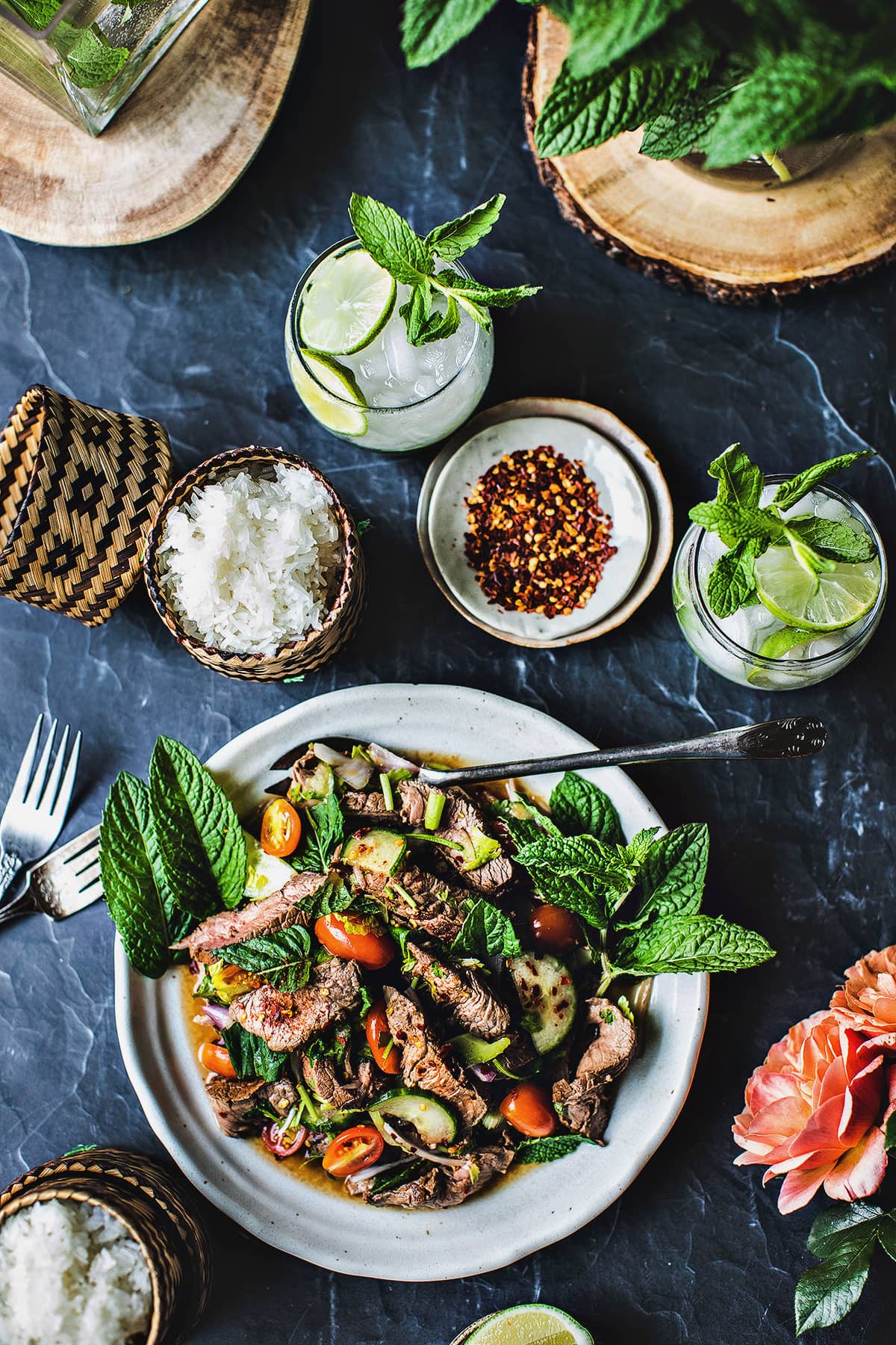 Thai beef salad on a plate with drinks, rice and garnishes. 