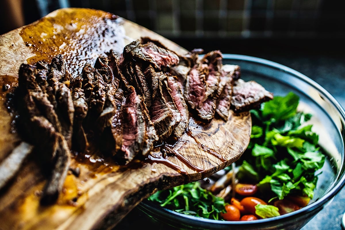 Sliced beef on a cutting board pouring over a bowl.