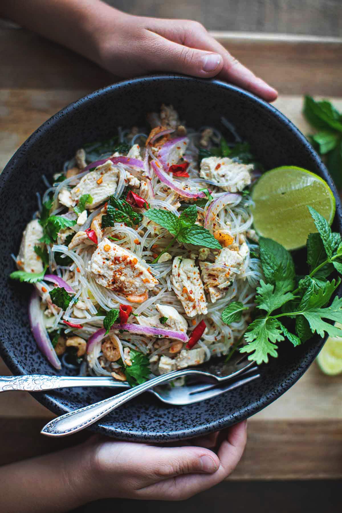 Two hands holding Yum Woon Sen Salad in a black bowl.