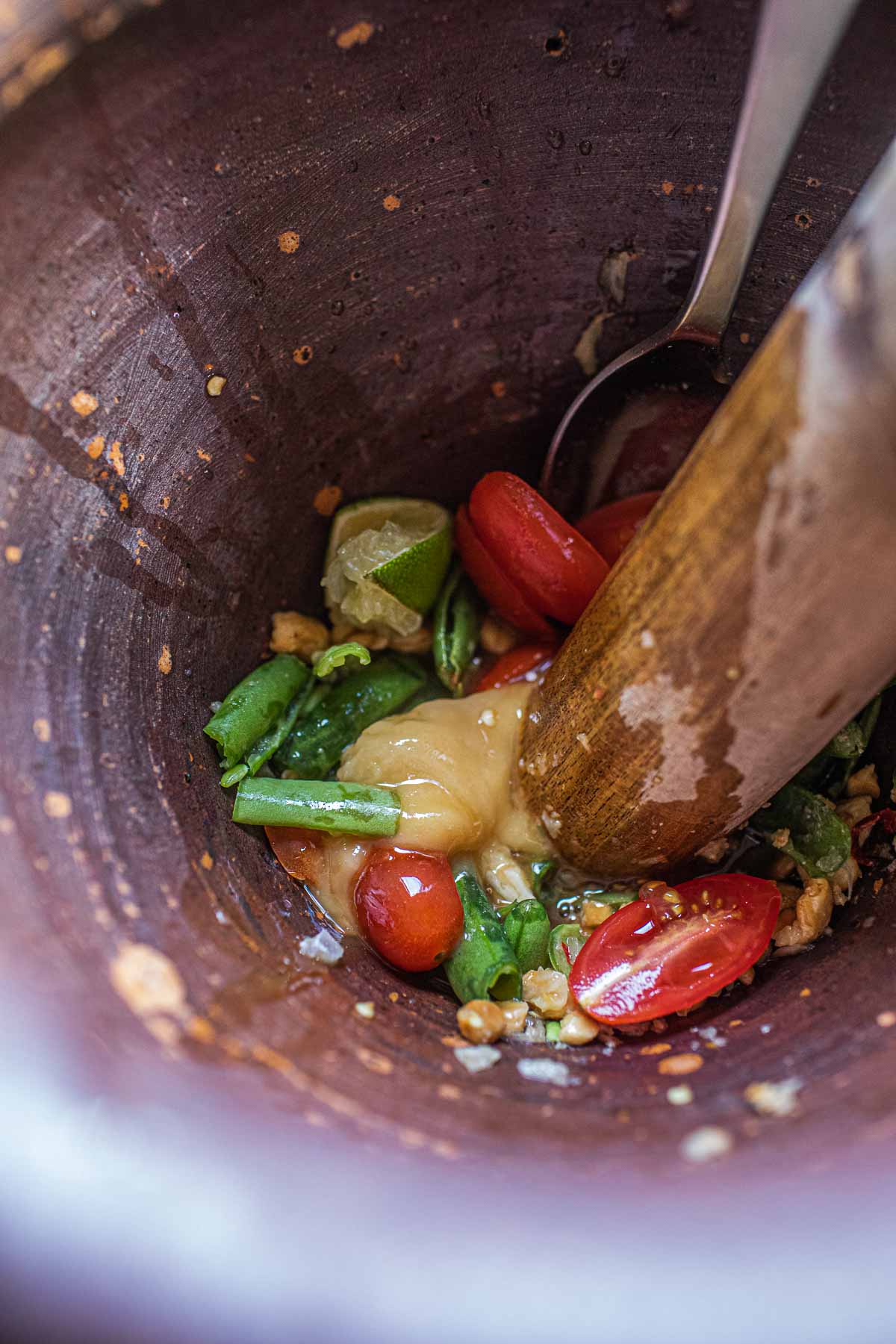 Beans, tomatoes, sugar, and sauces in a mortar and pestle for making papaya salad.