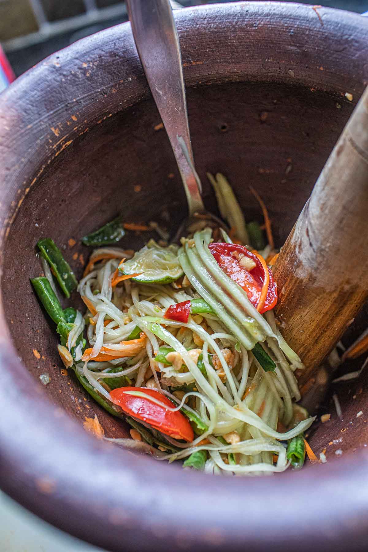 Papaya salad in a mortar with pestle inside. 