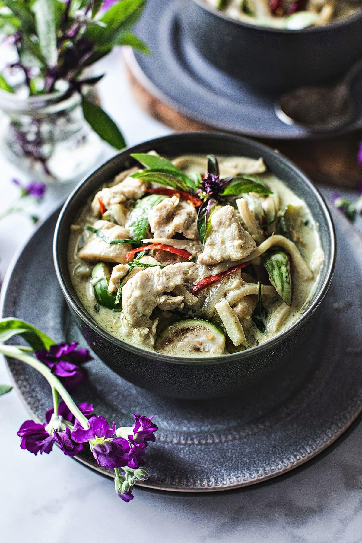 Green curry is a bowl over a plate with flower decoration.