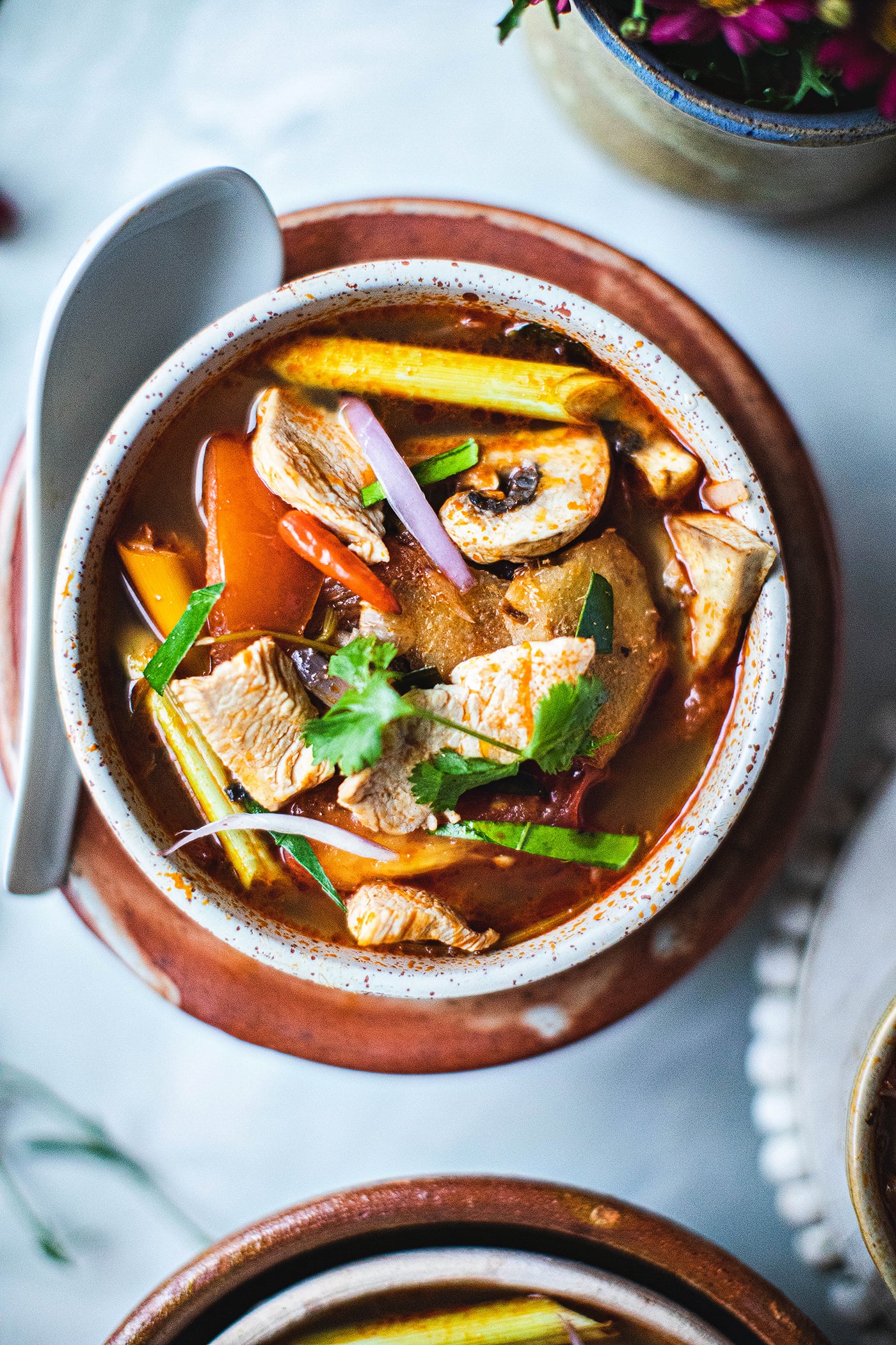 Tom yum soup with chicken in a small bowl with a spoon on the table