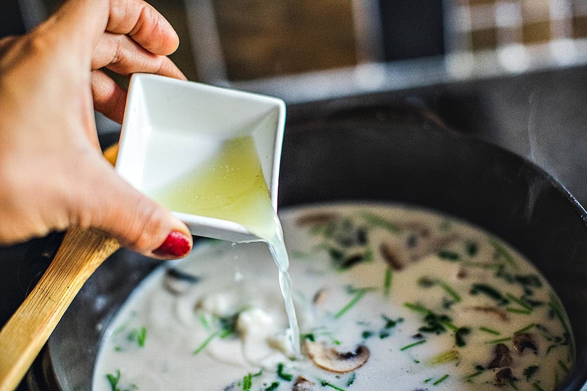 Lime juice pouring into a pot for Tom Kha soup.