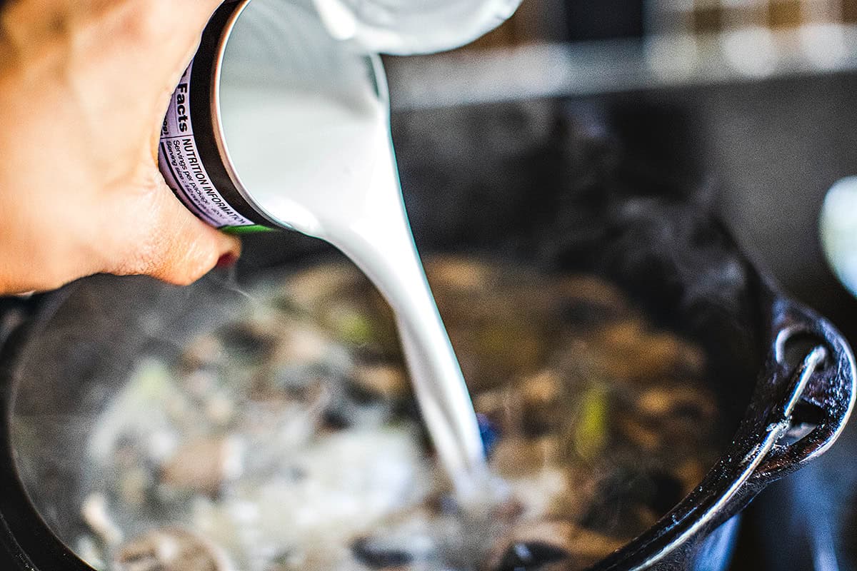 Coconut milk pouring into a pot for Tom Kha soup.