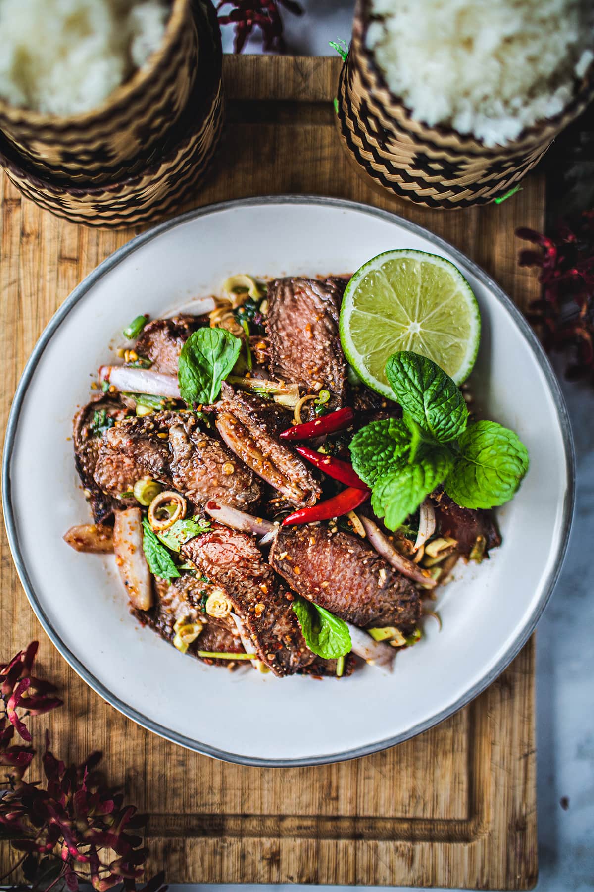 slices of grilled beef salad on a white plate with lime and mint garnish