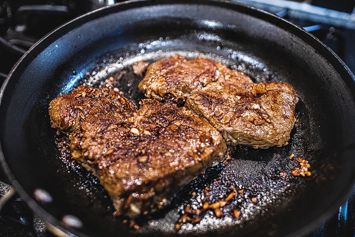 2 pieces of cooked steak on a stove top skillet
