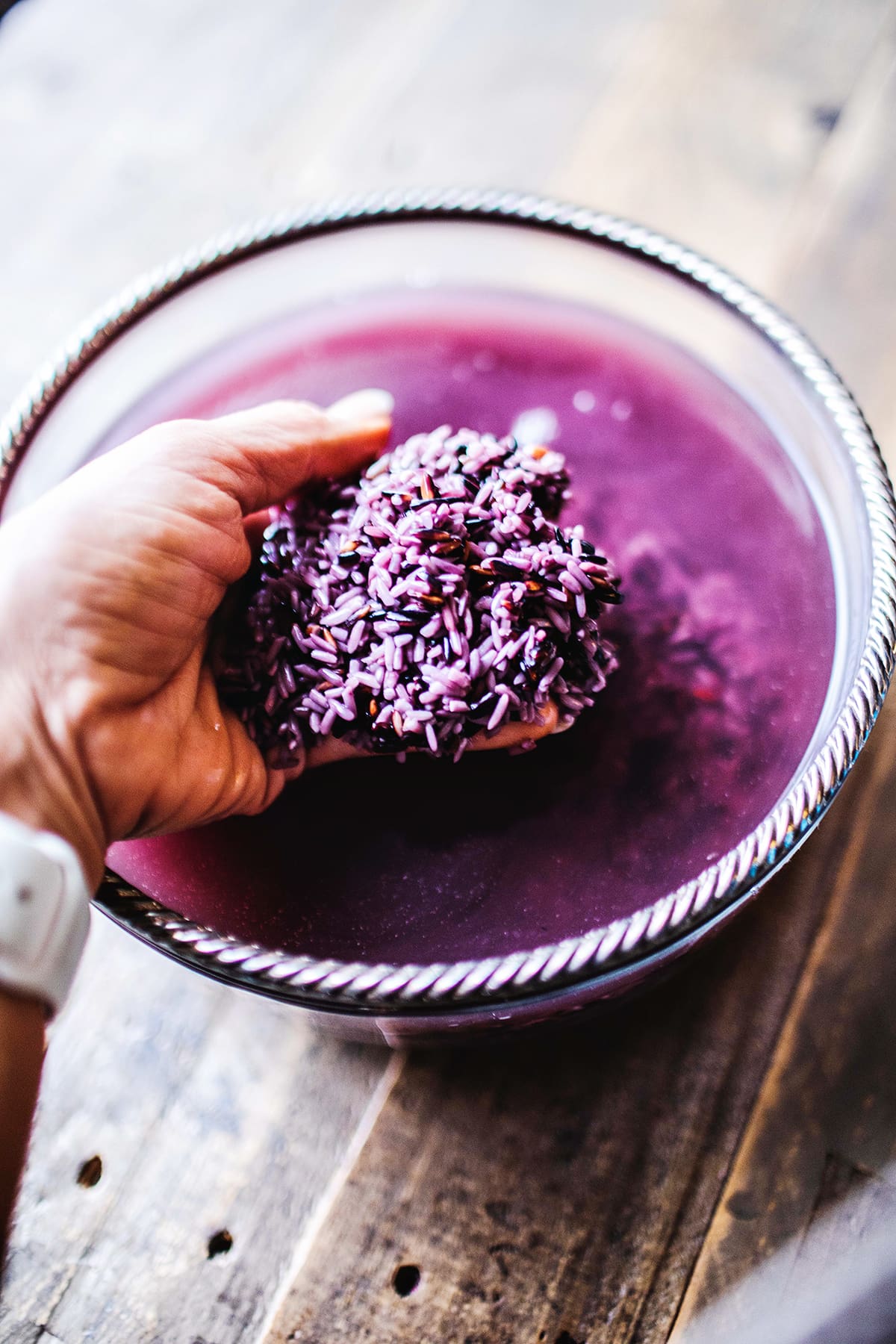 hand holding soaked purple rice grains over a glass bowl