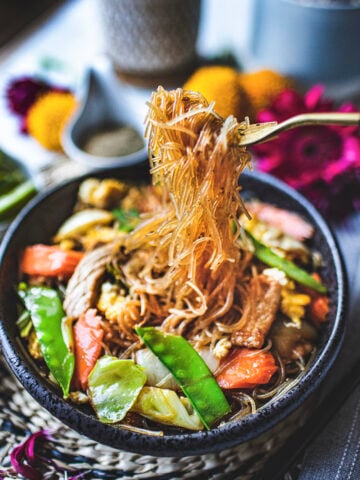 fork lifting noodles from a black bowl.