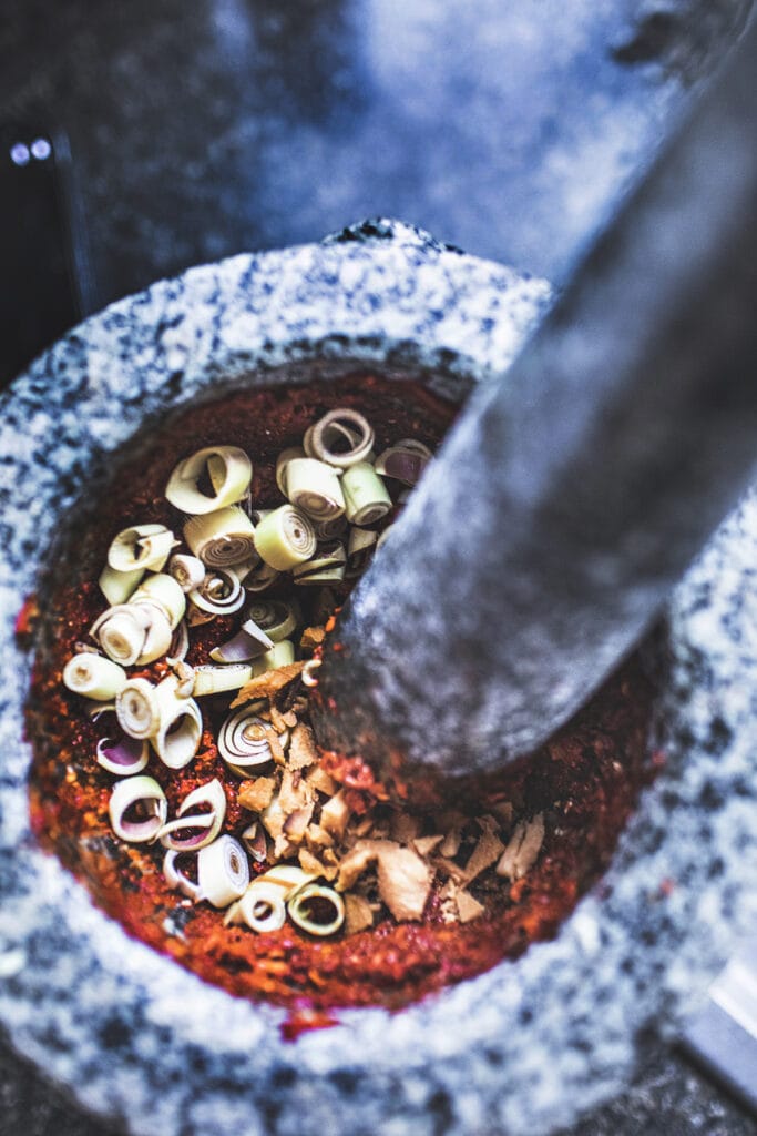 Chopped red chilis and lemongrass inside a stone mortar and pestle.