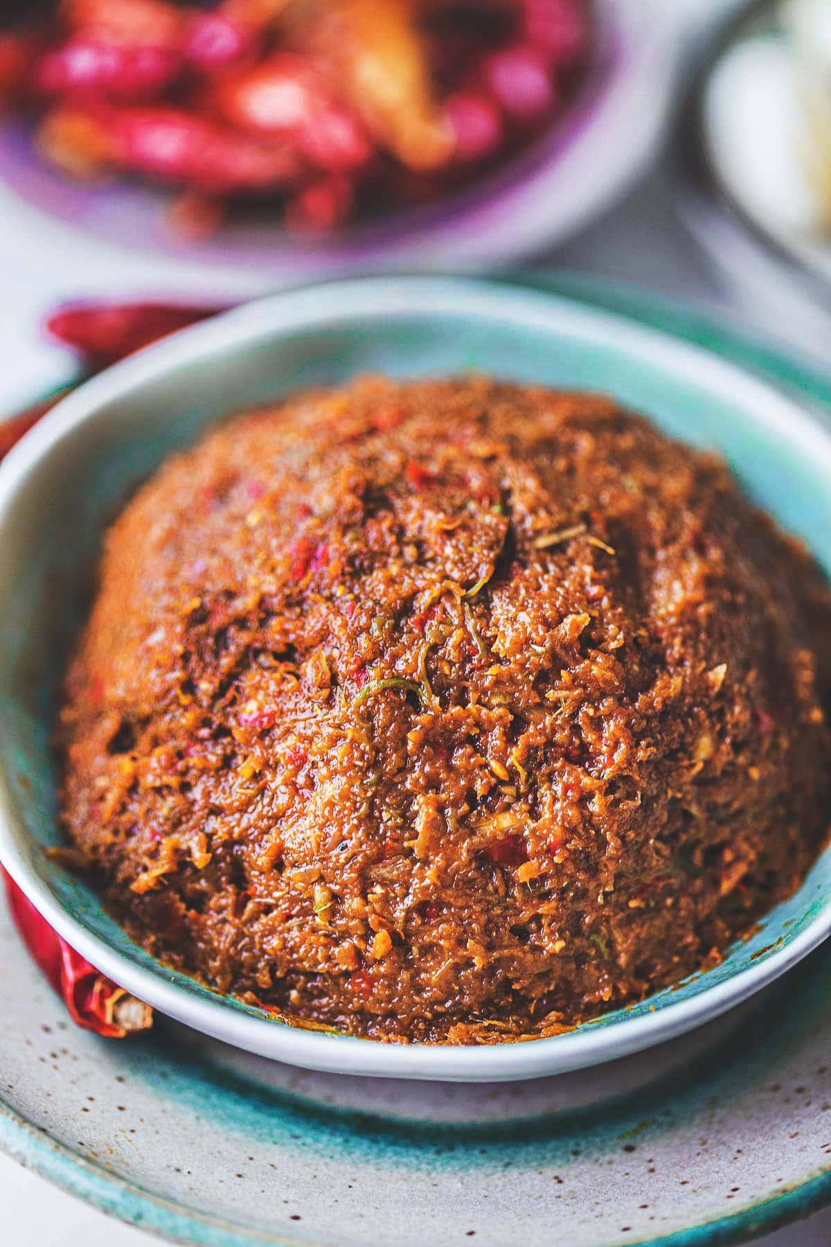 Prik king curry paste in a green bowl with red chilis on the side