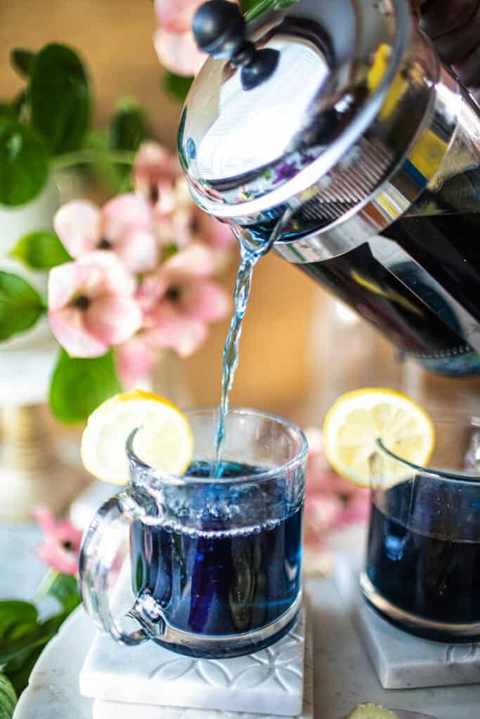 pouring blue tea from french press into a glass.