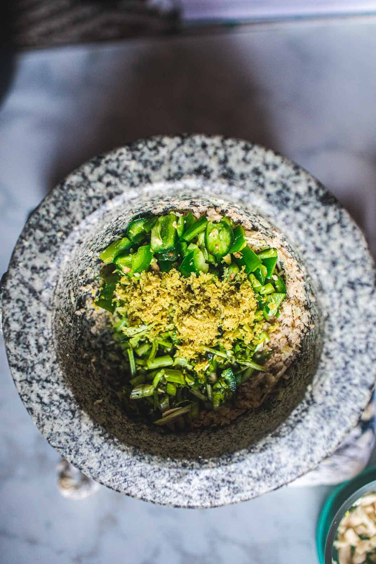 Green peppers and herbs in a mortar.