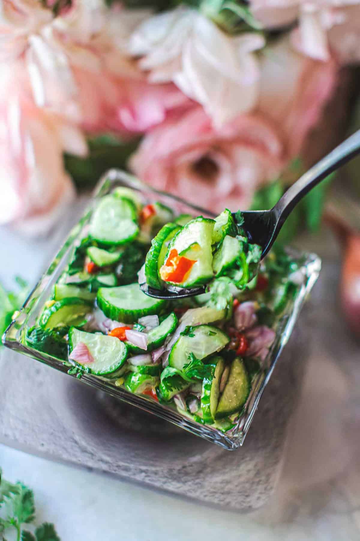 a spoon of cucumber salad over a square glass bowl