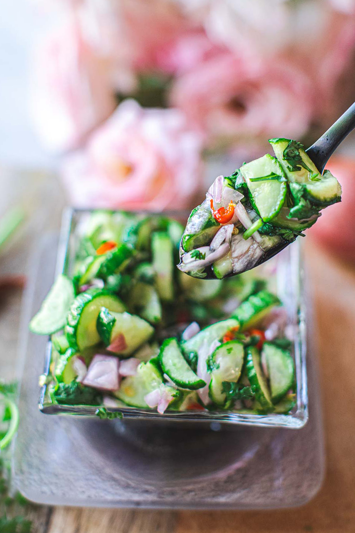 spoon lifting cucumber salad over a glass bowl