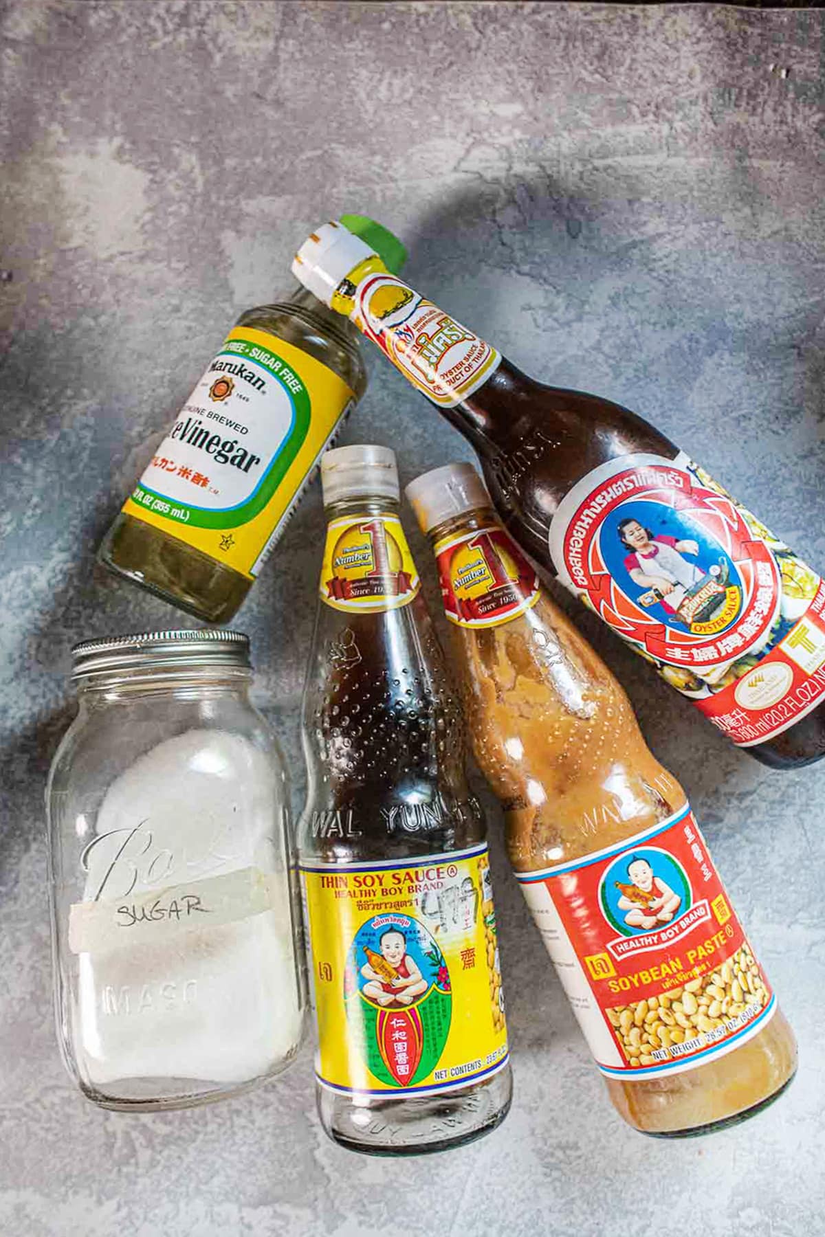 Rice vinegar, sugar, soy sauce, bean paste and oyster sauce bottles on counter.
