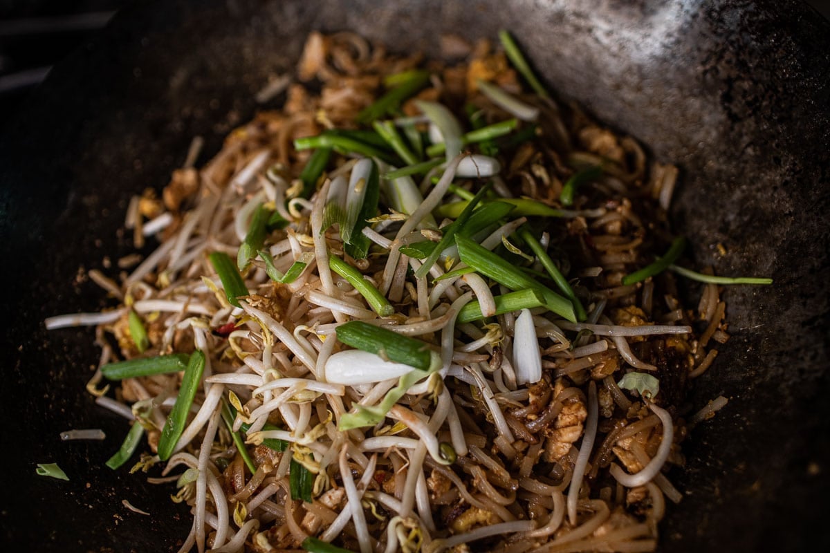 rice noodles, bean sprouts and green onions in a wok