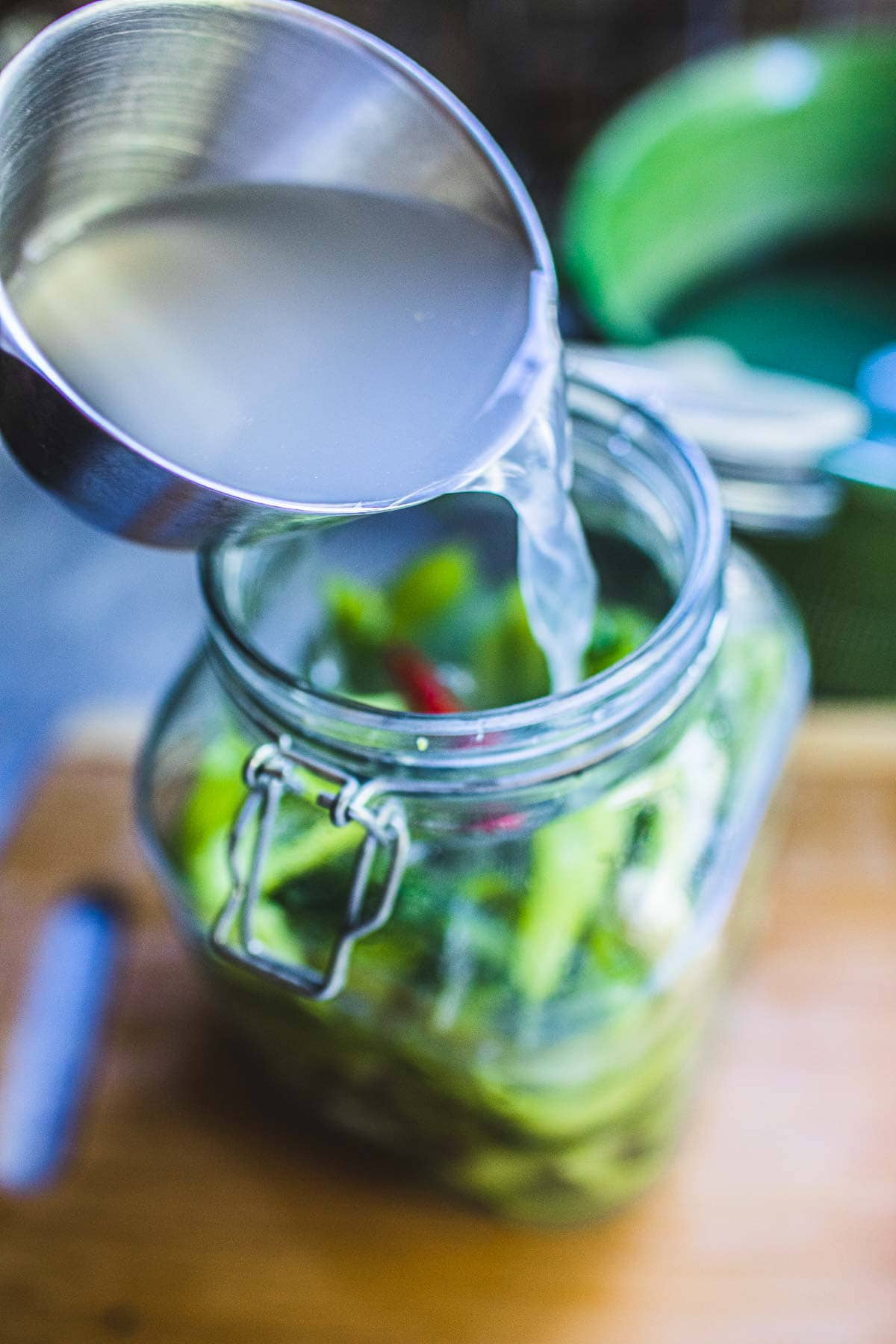 pouring liquid into pickled mustard greens in a glass jar