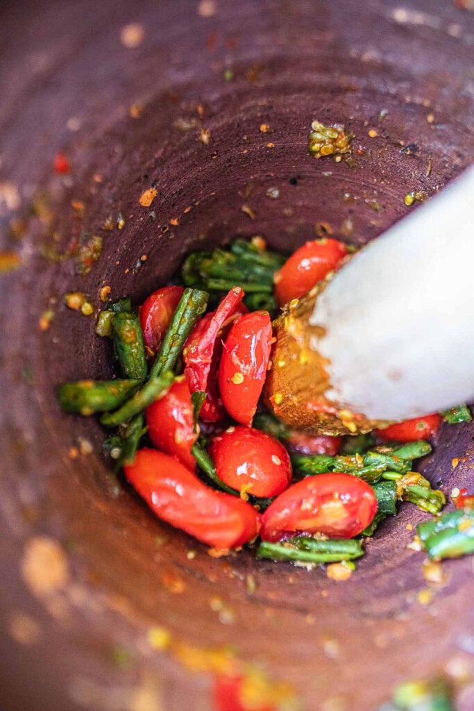 Tomatoes and beans pounded in mortar for Thai papaya salad.