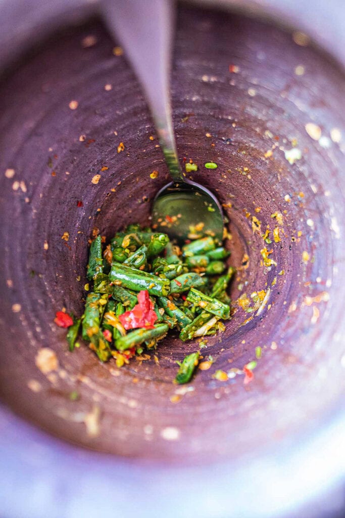 Green beans pounded in mortar with a spoon scooping it.
